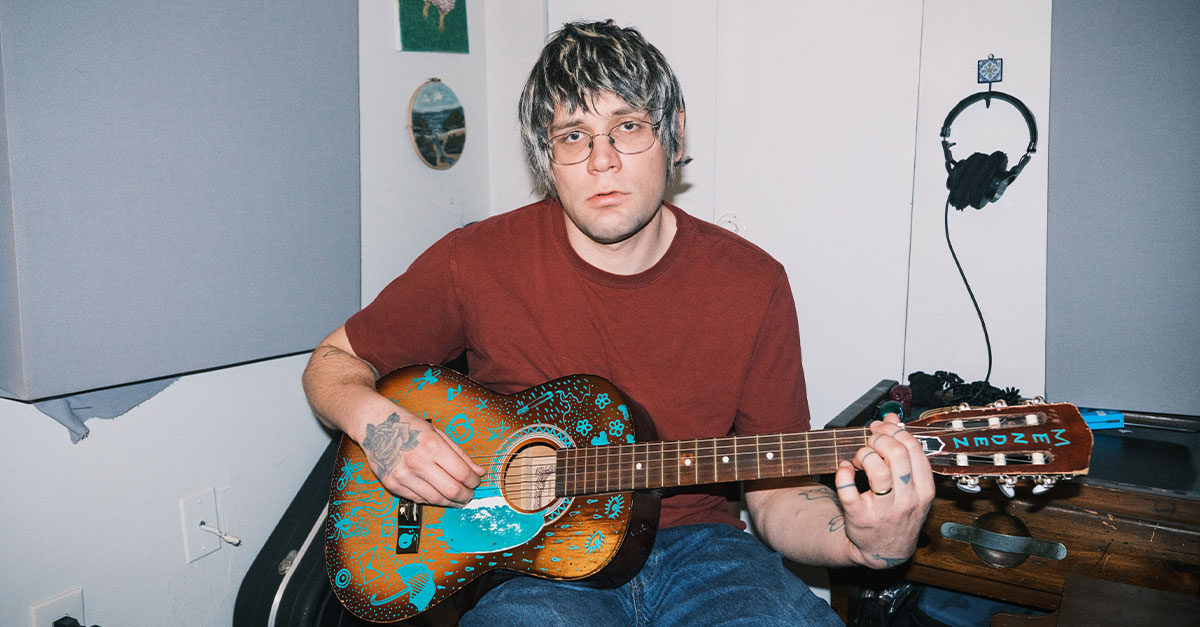A man holding a guitar sitting in his chair.